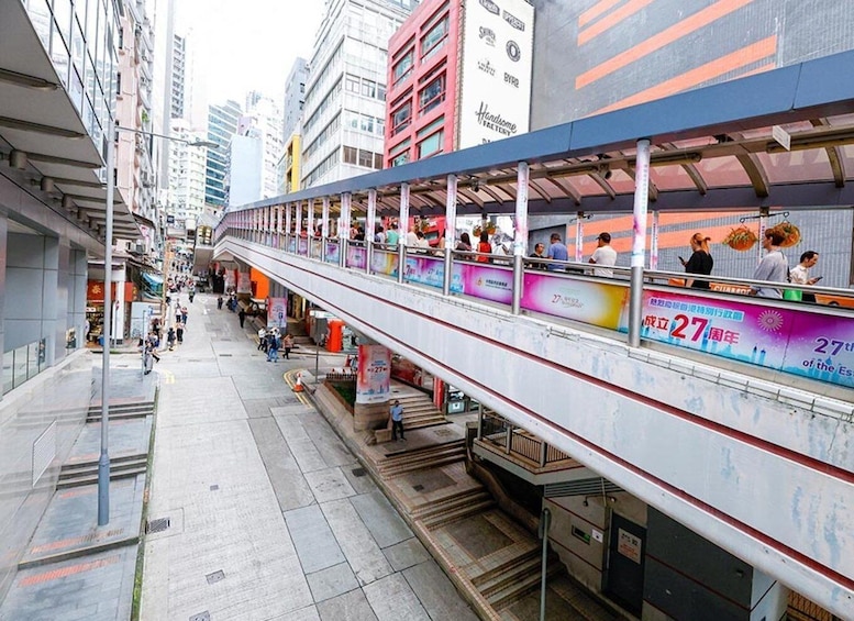 A pedestrian overpass with people walking, surrounded by urban buildings and advertisements. 2