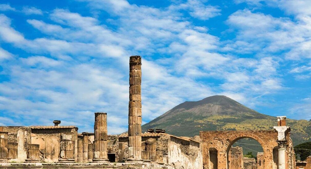 Ancient ruins with a tall column and an arched structure, set against a backdrop of a mountain and a clear sky. 4