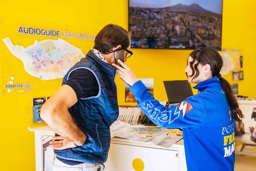 A person in a blue jacket with 'POWER' and 'FREE' text, standing at a counter with a map and brochures. 1