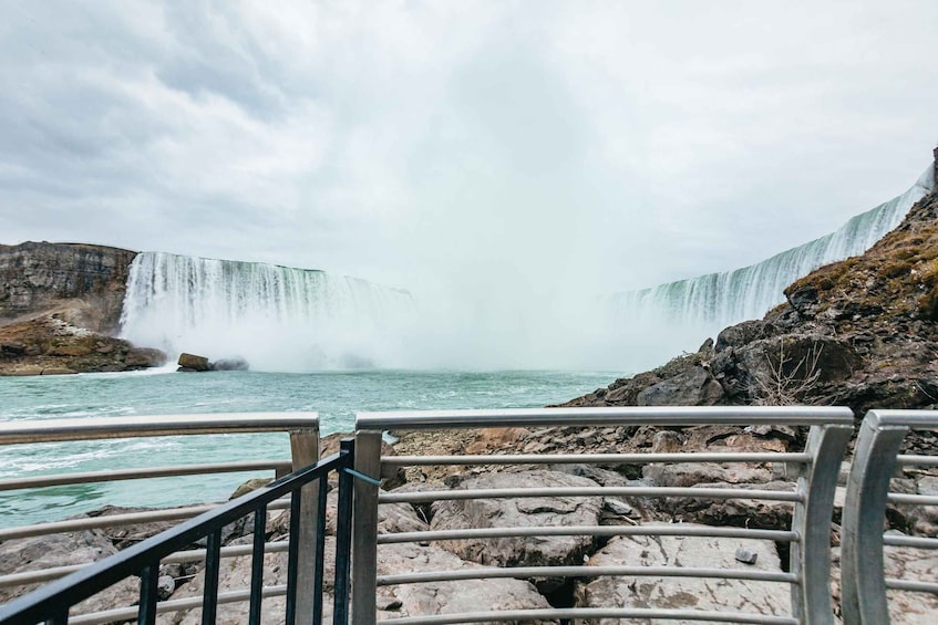 A waterfall cascading over a rocky cliff into a body of water, viewed from a railing. 3