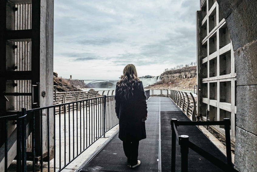 A person walking on a bridge with a waterfall in the background. 5