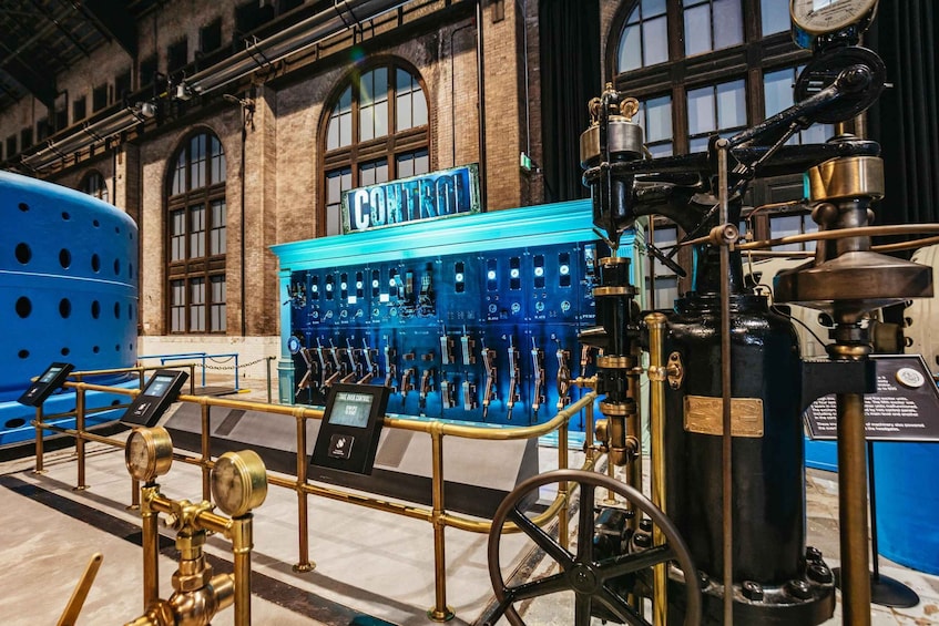A historical control panel with brass fittings and a blue control box labeled 'CONTROL' in front of a brick building with arched windows. 4
