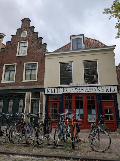 A street with a row of bicycles parked in front of a building with a sign reading 'RIJTUIG EN WAGENMAKERIJ VAN J.J. DE GROOT'. 4