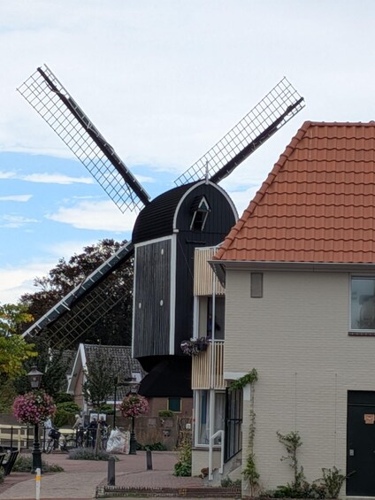 A traditional windmill with a black and white facade, a red-tiled roof, and a modern building with a beige facade in the foreground. 2