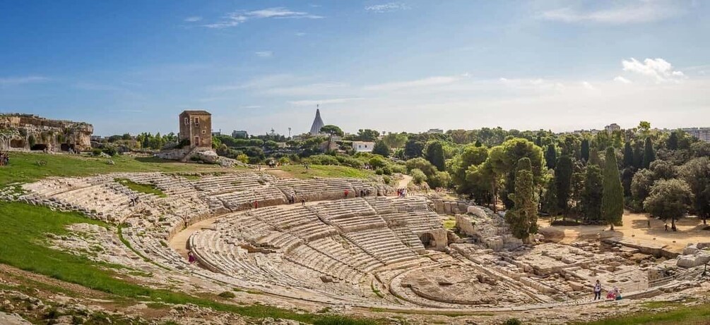 An ancient amphitheater with tiered seating and a small tower in the background. 2
