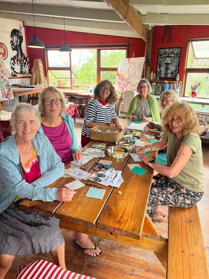 A group of people engaged in painting at a wooden table in a room with red walls and large windows. 1