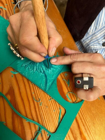 Hands using a tool to cut green material on a wooden surface. 3