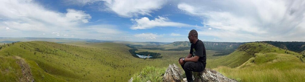 A person sitting on a rock overlooking a valley with a lake. 4