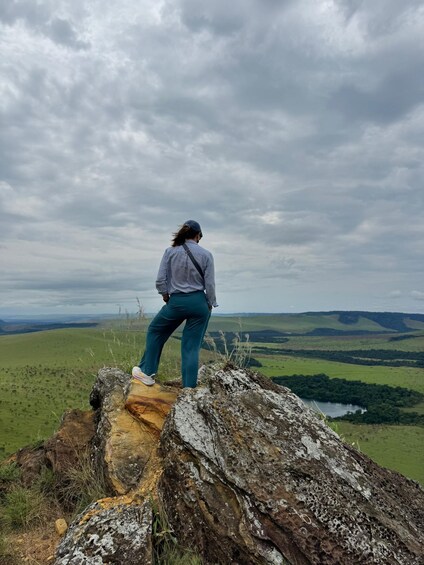 A person standing on a rock with a view of green hills and a lake. 2