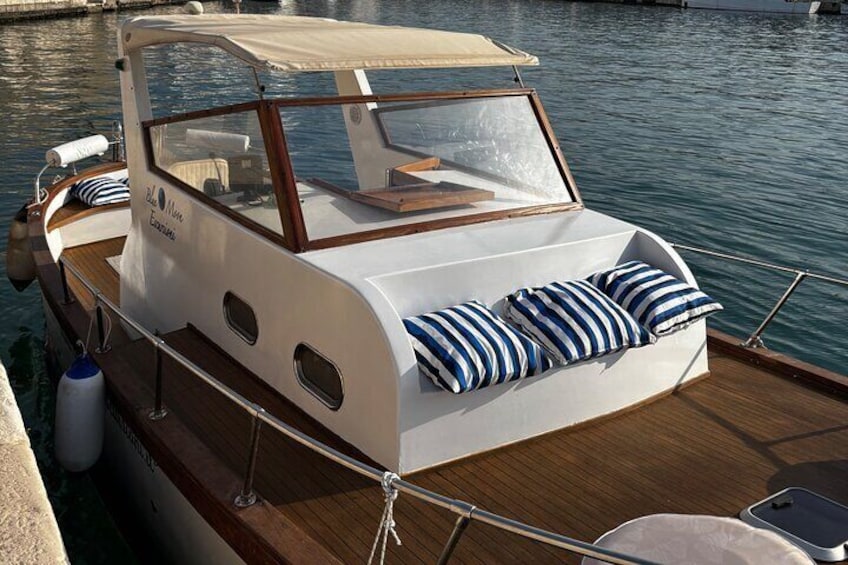 Een klein bootje met een witte hut en blauw gestreepte kussens, afgemeerd in een jachthaven. 1