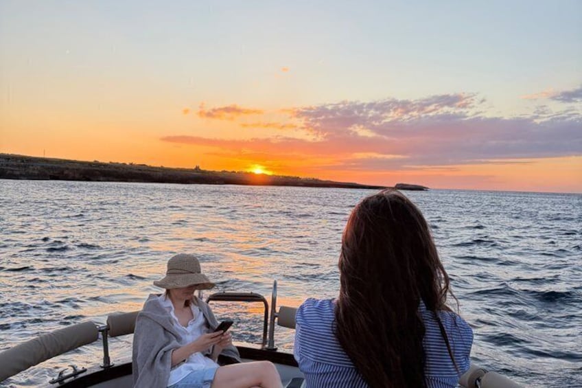 Twee mensen op een boot bij zonsondergang, met de zon die achter de horizon verdwijnt. 3