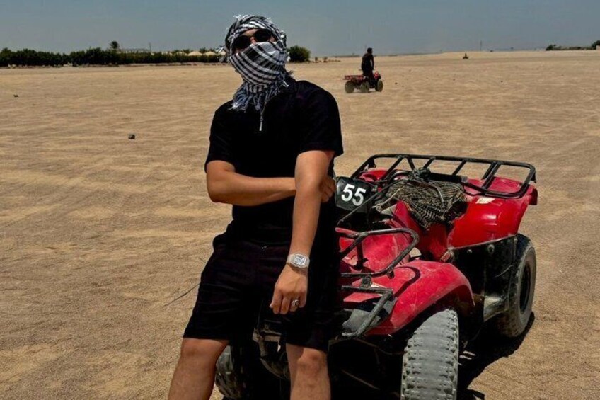 A person sitting on a red ATV with the number 55, in a barren, sandy landscape. 2