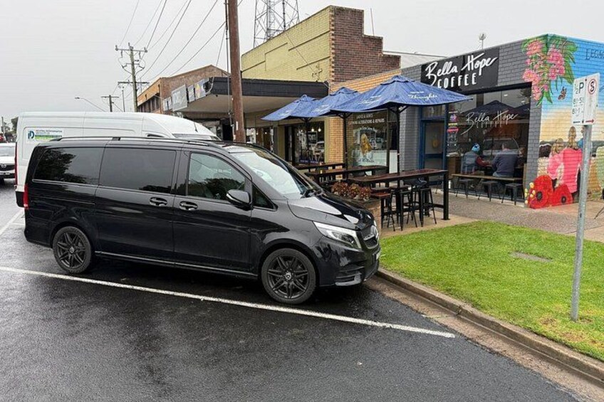 En svart skåpbil stod parkerad på en våt gata, ett kafé med uteservering och en väggmålning prydde byggnaden. 3