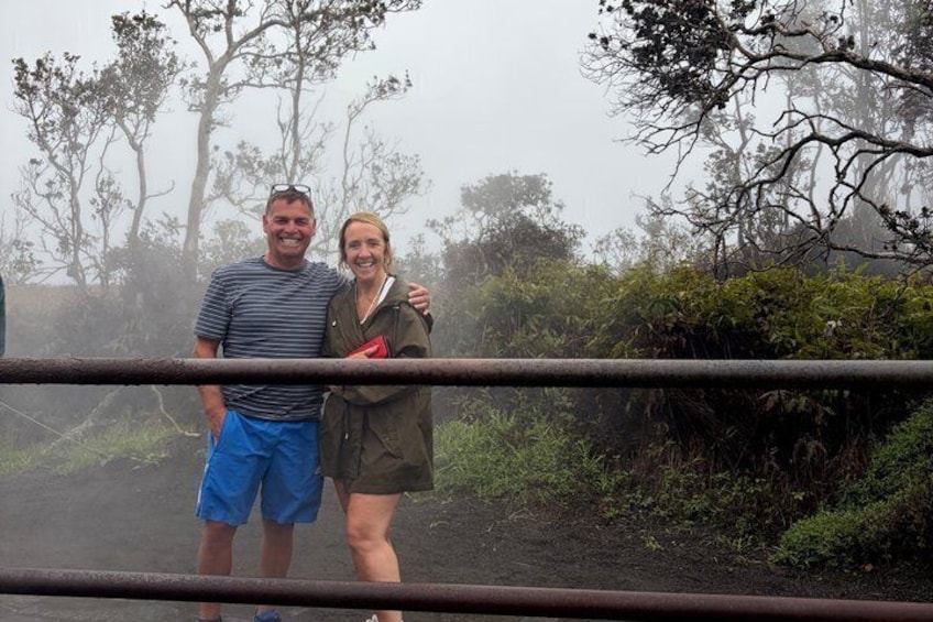 Two people standing by a metal railing with a forested background. 3