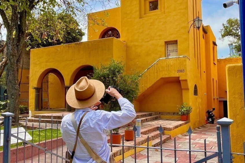 Une personne prend une photo d’un bâtiment jaune orné d’arcades, sur lequel on peut voir le numéro 2083. 1