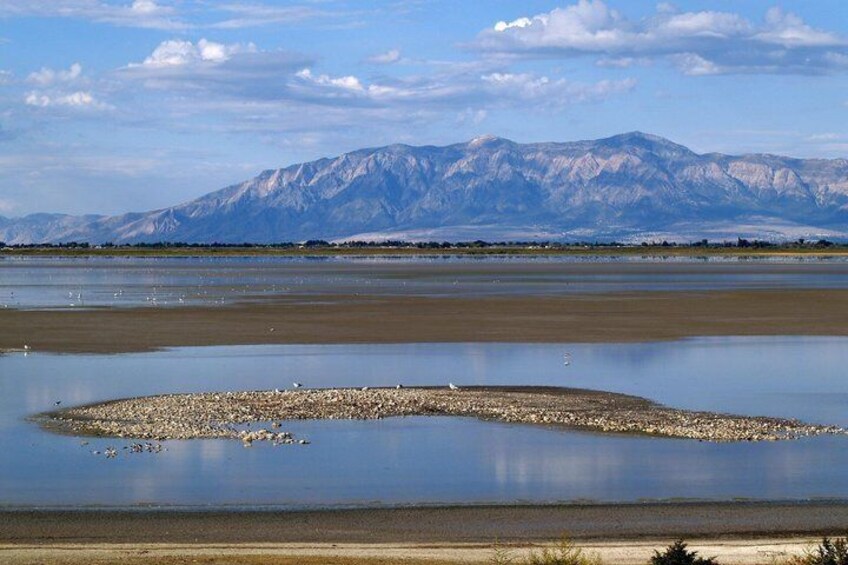 A calm lake with a rocky island in the center, surrounded by mountains under a clear sky. 2