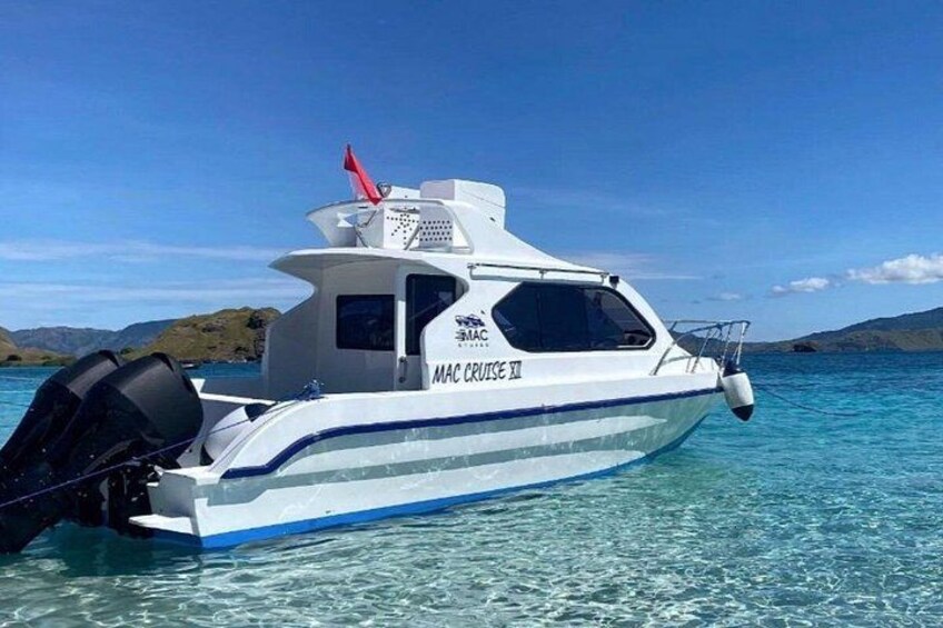 En vit och blå motorjakt med namnet ”MAC CRUZE II” glider fram på det klara, turkosfärgade vattnet, med ett bergigt landskap i bakgrunden. 4