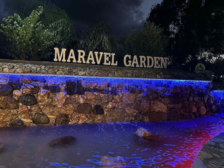Muro de piedra con una fuente de agua y el texto 'MARAVEL GARDEN' iluminado en azul. 1