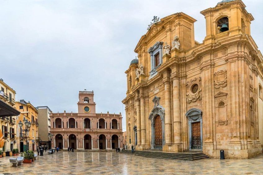 A historic plaza with a large church featuring arched doorways and a bell tower. 1