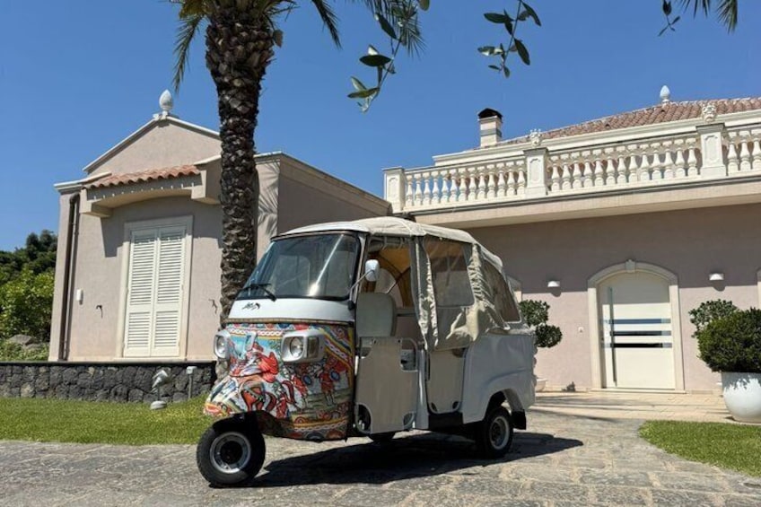 Une voiture ancienne est garée devant une maison de style méditerranéen, avec un palmier et un ciel d’un bleu éclatant. 1