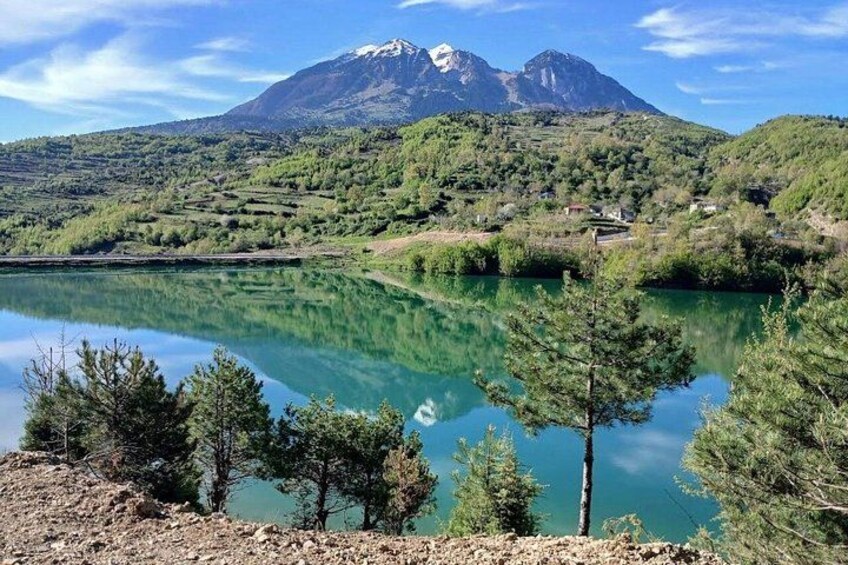 Un lago dalle acque limpide che riflette il paesaggio circostante, tra alberi e una montagna con cima innevata. 3