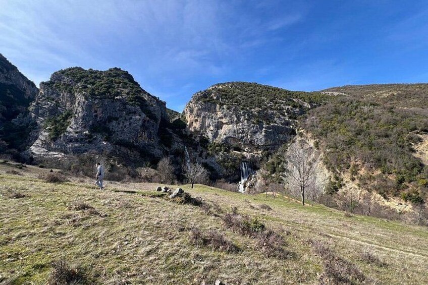 Paesaggio montuoso con una cascata, una persona che cammina e cielo sereno. 4