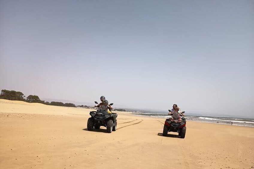 Dos personas paseando en cuatrimotos sobre una playa arenosa con el océano al fondo. 1