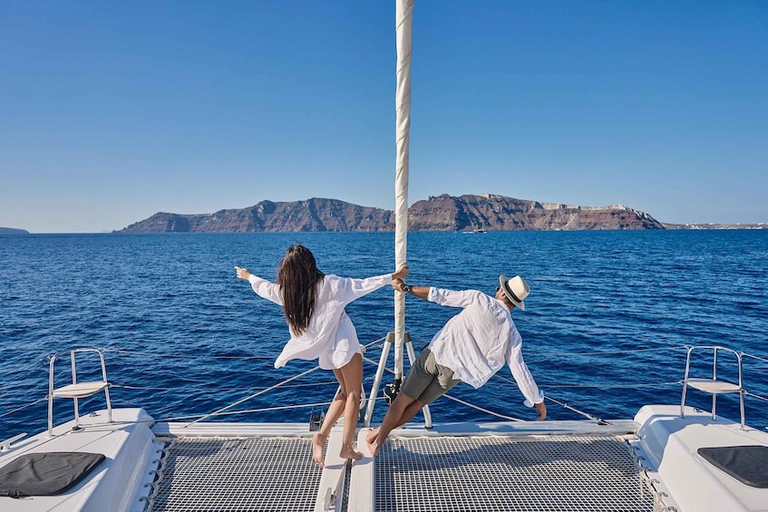 Two people on a sailboat with a mountainous coastline in the background. 5