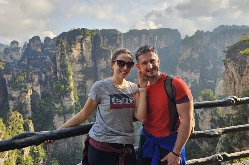 Two people standing on a wooden platform with a mountainous landscape in the background. 4