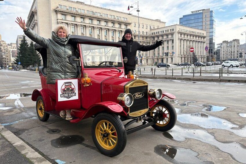 Un coche antiguo con un hombre y una mujer de pie sobre él, un cartel que dice 'Retro Tours' y un paisaje urbano al fondo. 5