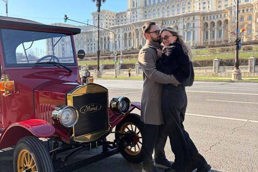 Un coche Ford Modelo T antiguo, una pareja abrazándose y un edificio imponente al fondo. 2