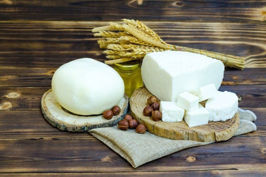 Un piano di legno con un formaggio stagionato intero, un tagliere con cubetti di formaggio e una bottiglia d'olio d'oliva. 3
