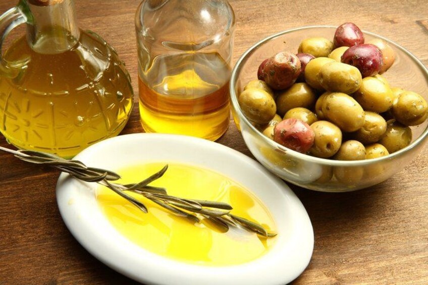 Un tavolo di legno con un piatto bianco contenente olio d'oliva, una ciotola di vetro piena di olive e una bottiglia di olio d'oliva. 4