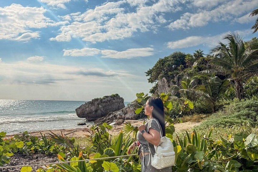 Eine Person steht an einem Strand mit einem Felsen und Palmen im Hintergrund. 5