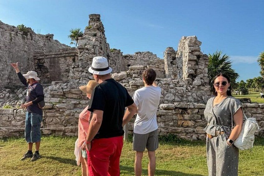 Touristen betrachten alte Ruinen mit Steinstrukturen und Palmen im Hintergrund. 4