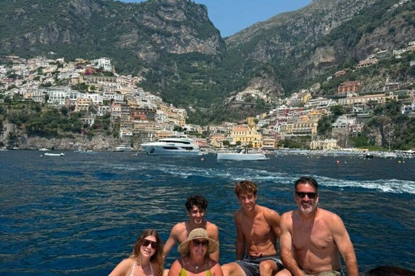 Un grupo de personas en un barco, con un pueblo costero y montañas al fondo. 5