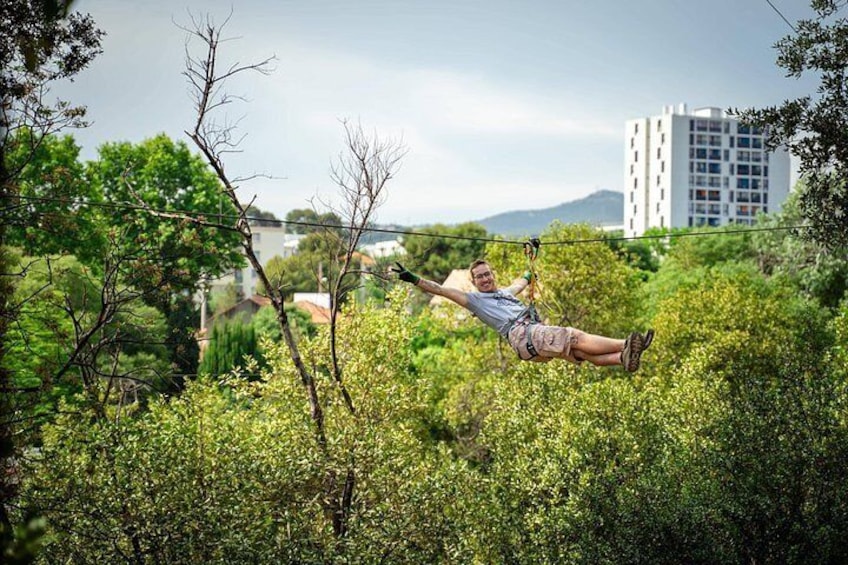 Una persona che si dondola su una corda in mezzo a una fitta vegetazione verde, con un edificio sullo sfondo. 1