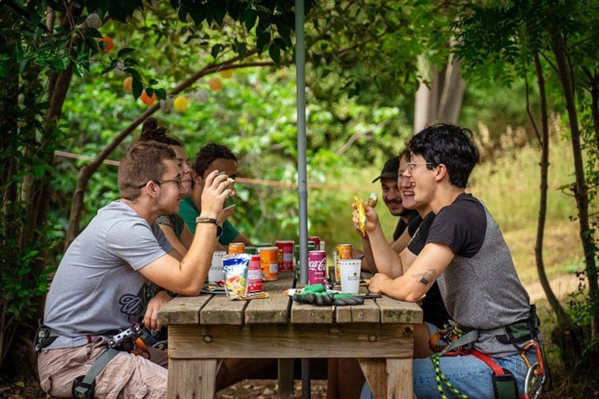 Un gruppo di persone sedute a un tavolo di legno all'aperto, circondate dal verde. 5