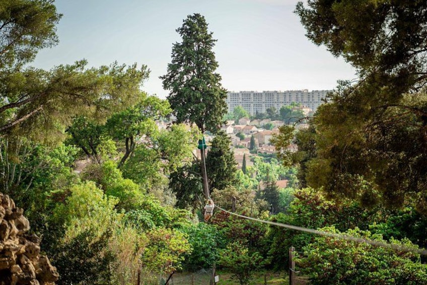 Una persona su un ponte sospeso sopra una zona boschiva, con edifici sullo sfondo. 4
