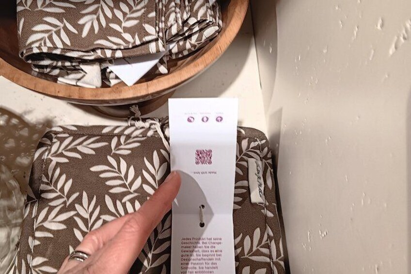 A hand holding a paper with a QR code, next to a patterned fabric. 3