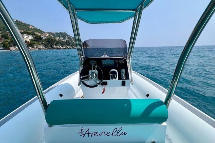A boat named 'l'Arenella' with a steering wheel, dashboard, and a view of the sea and a coastline. 1