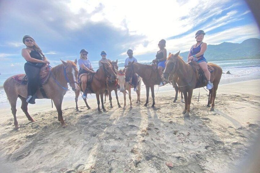 Un grupo de personas montando a caballo en una playa, con el océano y montañas al fondo. 5