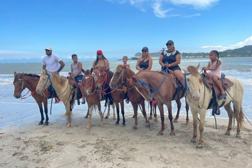 Un grupo de personas montando caballos en una playa, con el océano y un cielo despejado al fondo. 2