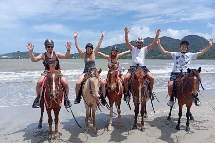 Cuatro personas a caballo en una playa, con olas al fondo. 1