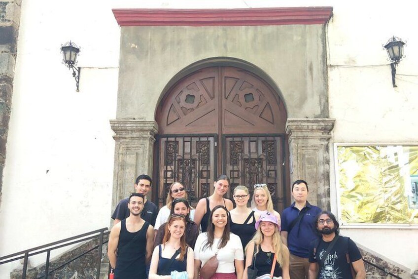 A group of people standing in front of a building with a large wooden door and a red roof. 2