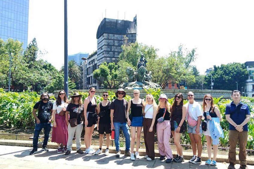 A group of people standing in a park with a statue and modern buildings in the background. 3