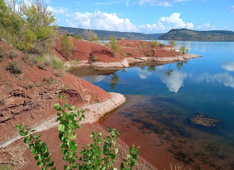 A calm lake with red earth mounds and green vegetation in the foreground. 4