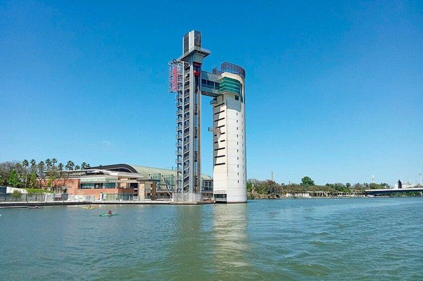 Een hoog gebouw met een cilindrische basis en een rechthoekig bovenstuk, gelegen aan een kalm waterlichaam. 2
