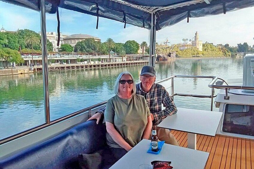 Een bootje met twee personen aan een tafel, een wateroppervlak en een gebouw in de verte. 4