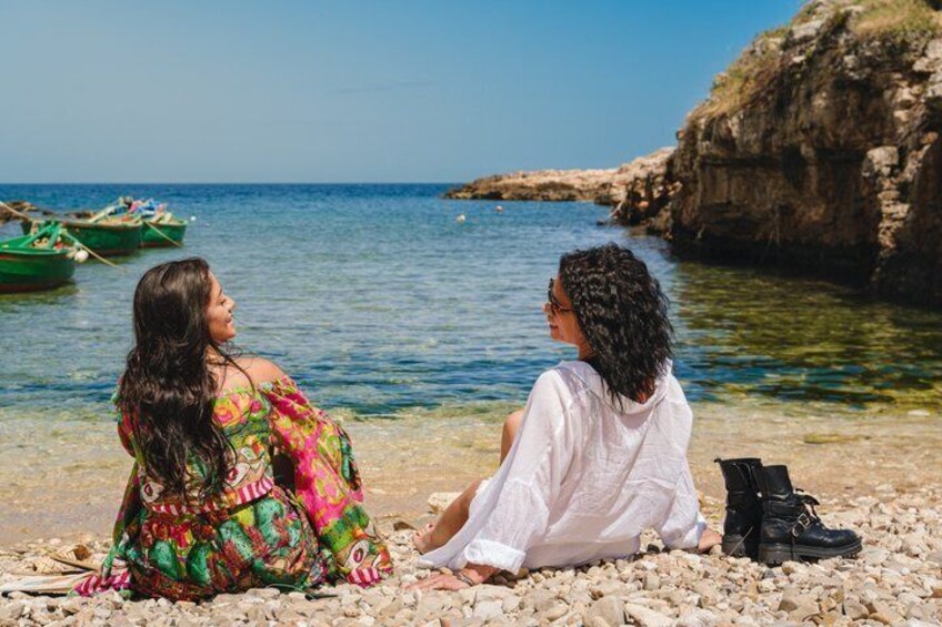 Zwei Personen sitzen auf Kieselsteinen am Meer, im Hintergrund Schiffe. 5